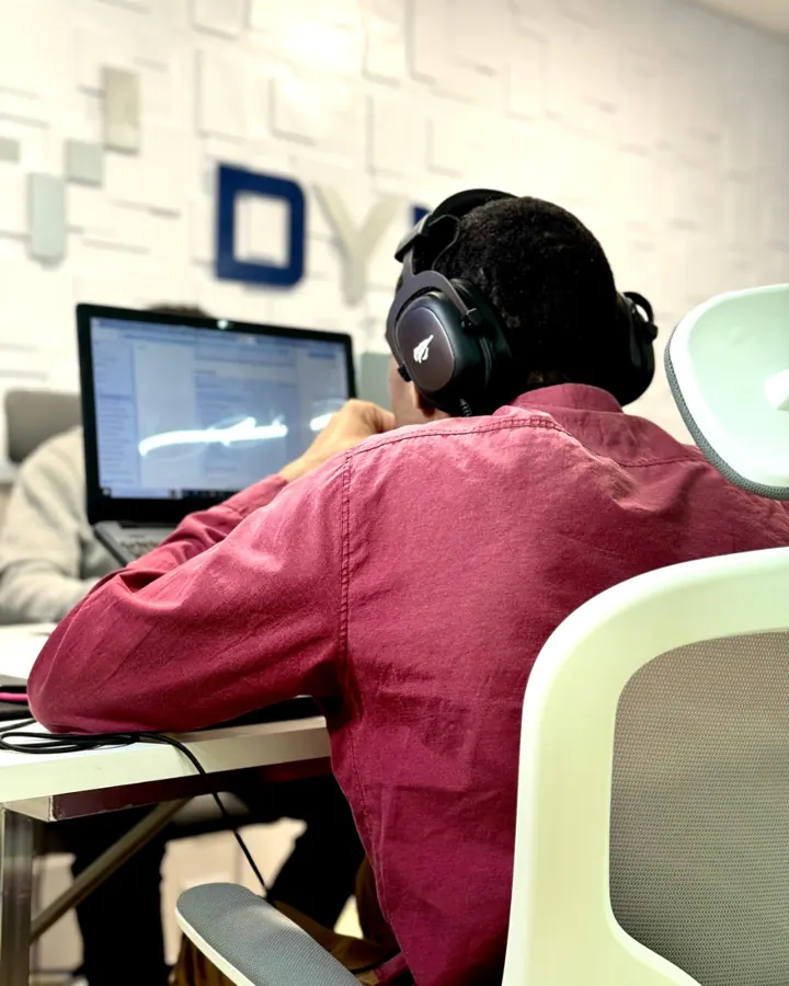 Analista da Dyna Tecnologia com headset acompanhando o desenvolvimento em dois monitores